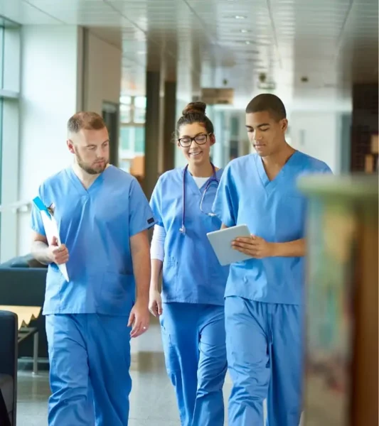 Una persona con guantes médicos azules utiliza un paño de limpieza amarillo para limpiar una superficie metálica reflectante en lo que parece ser un entorno sanitario o de laboratorio, con equipos científicos difuminados en el fondo.